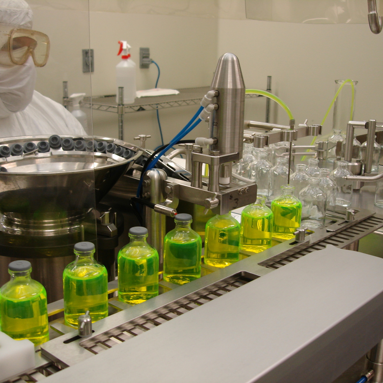 A sterile vial fill line with green drug product being dispensed