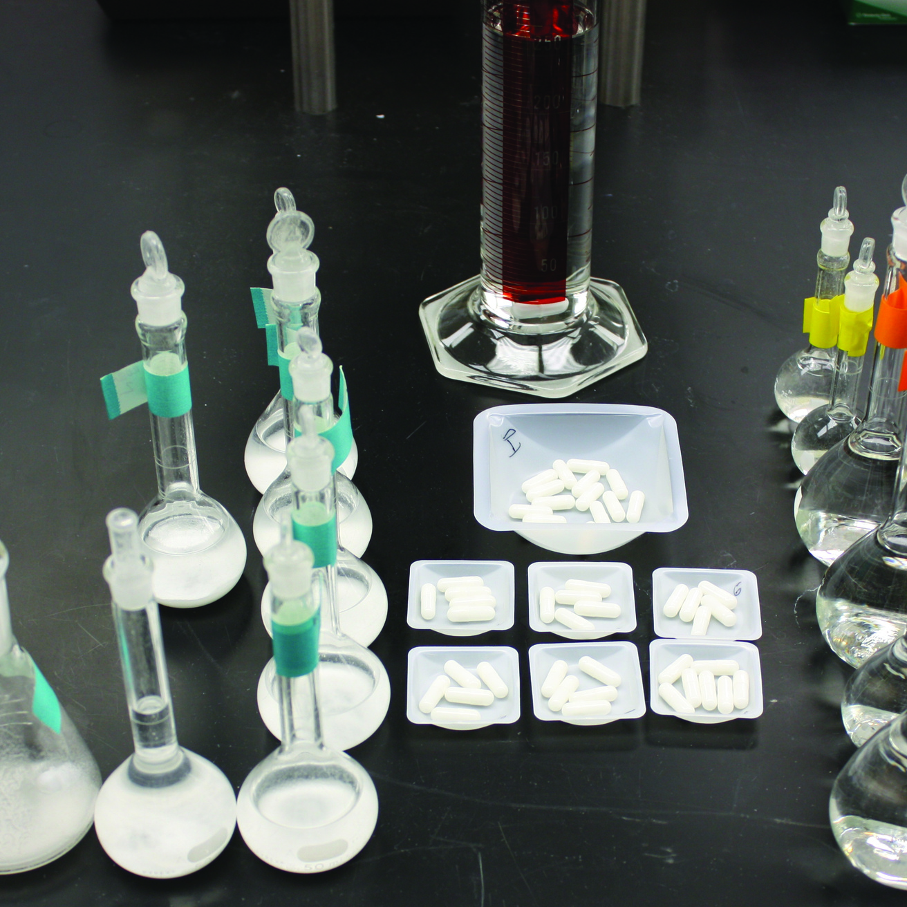 collection of vials of solid drugs, pills, and vials of liquid on a black lab bench