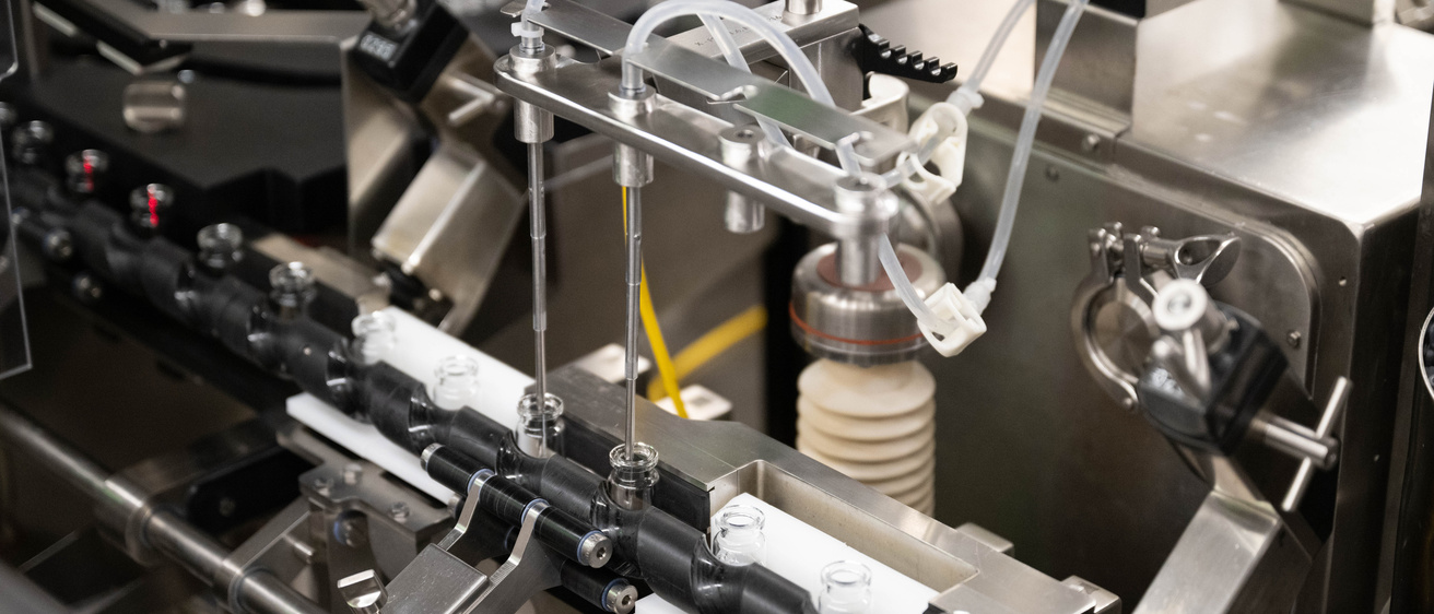 Automated pharmaceutical filling machine dispensing liquid into small glass vials on a production line.