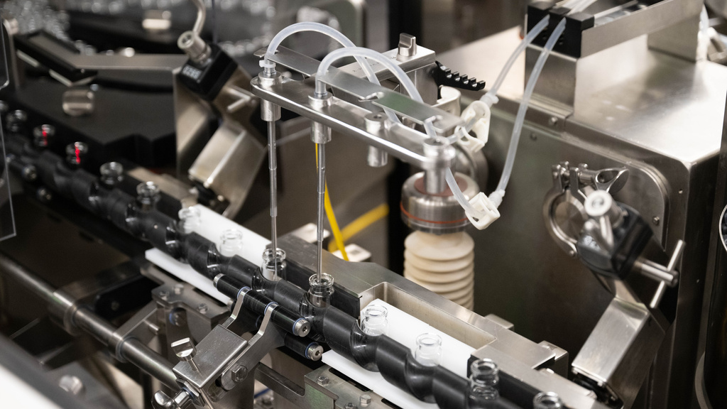 Automated pharmaceutical filling machine dispensing liquid into small glass vials on a production line.
